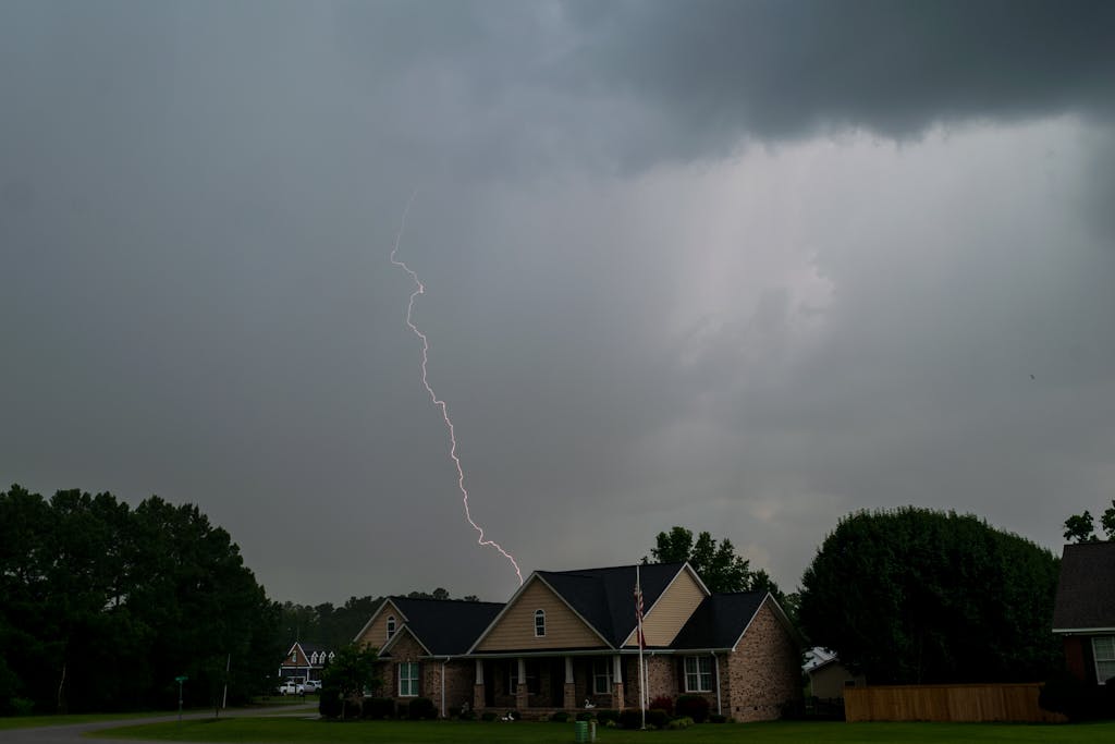 A vivid lightning bolt pierces the sky over suburban houses during a storm, capturing nature's raw power.